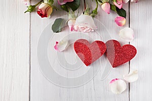 Pink rose flowers petals and handmade wooden glitter hearts on white rustic wood