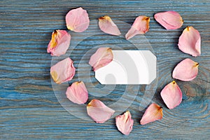 Pink rose petals imaging heart shape on blue wooden board with blank white card inside