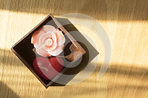 Pink rose and red heart scented aroma candle in wooden box on wooden background with light and shadow from window .spa concept