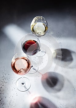 Pink rose,red and white wine glasses on light background with shadows