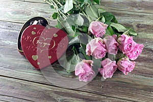 Pink roses and box with sweets on a wooden table