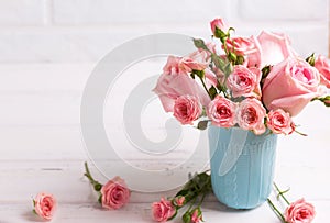 Pink roses flowers in blue cup against white brick wall.