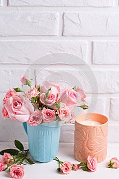 Pink roses flowers in blue cup and burning candle against whit