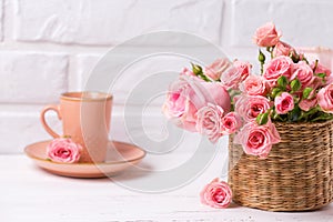 Pink roses flowers and cup of coffee against white brick wall