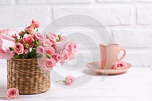 Pink roses flowers and cup of coffee against white brick wall.