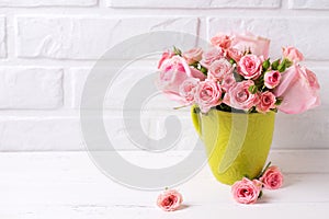 Pink roses flowers in green cup against white brick wall.