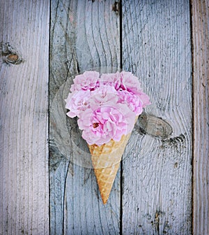 Pink roses flowers in ice cream cone on rustic wooden background