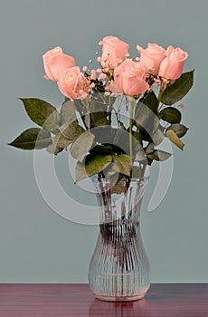 Pink roses with green leaves in a glass vase with water on a bro