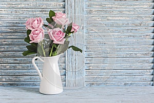 Pink roses in white enamel jug on a blue rustic background. Free space for text.