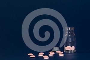 Pink round tablets, clear small medicine bottle on dark blue background