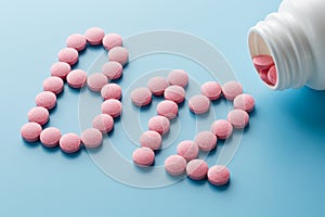 Pink round vitamins B12 shaped pills on a blue background spilled from a white can