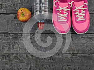 Pink running shoes for fitness classes at the gym and a ripe Apple on a wooden floor. View from above.