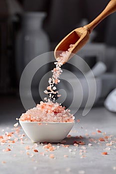 Pink salt in crystals is poured into a small white bowl