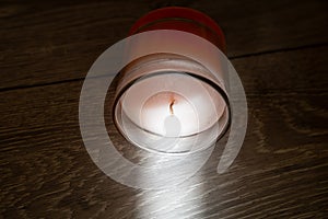 pink scented candle in a glass cover on a wooden background, sunbeam light creates creative effect of burning candle