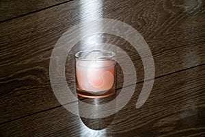 pink scented candle in a glass cover on a wooden background, sunbeam light creates creative effect of burning candle, therapy