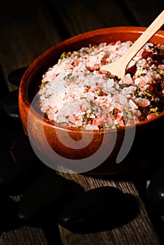 Pink sea salt with herbs and stones on wooden board