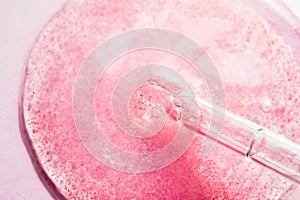 Pink serum, cosmetic fluid with pipette on bright background. Beauty product with peptides, ceramides, hyaluron gel