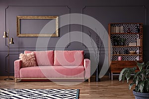 Pink settee against grey wall with mockup of gold frame in elegant living room interior. Real photo