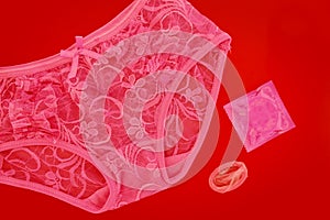 Pink women`s lace panties with condom on red background