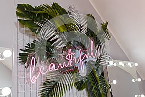 Pink shining neon inscription Beautiful on artificial tropic plant leaves, room interior decoration, lights bokeh, mirror