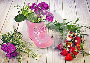 Pink shoe and bouquet of summer wildflowers, ripe red strawberries on the table. Hello summer