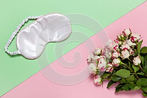 Pink silk sleep mask, bouquet of small roses on pastel two-color background pink and green, copy space, flat lay. March 8,