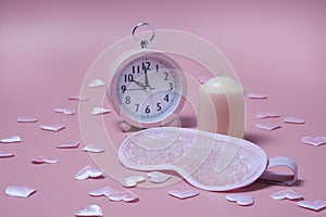 Pink sleep mask, alarm clock and candle on pink background with small hearts