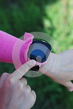 Pink Smartwatch Phone girl's Hand. Kid Using pink Intelligent Phone. Summer time Otside.