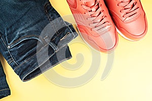 Pink sneakers and jeans on pastel yellow background. Concept of sport and healthy lifestyle.