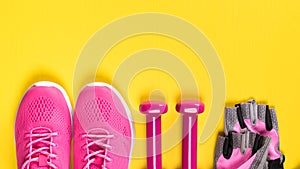 Pink sneakers, gloves and dumbbells lie in a row on a yellow background, a place for an inscription