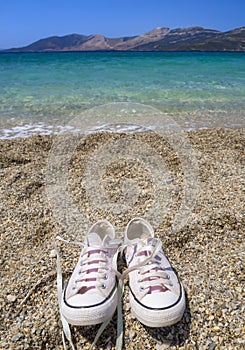 Pink sneakers stand on the Sunny beach of the Aegean sea on the island of Evia in Greece