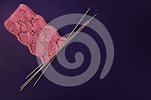 Pink socks made of wool, knitted with an openwork pattern on four knitting needles on dark purple background