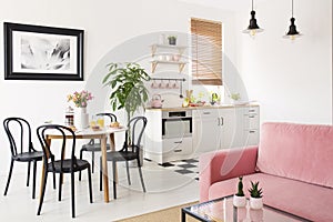 Pink sofa in white apartment interior with kitchenette and black chairs at dining table. Real photo photo