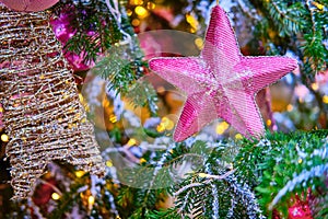 Pink soft star hanging as decoration on a snow covered Christmas tree, close-up