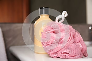 Pink sponge and shower gel bottle on washbasin in bathroom, closeup. Space for text