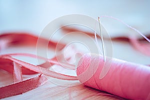 Pink spool of thread and a needle in it, side view on the table