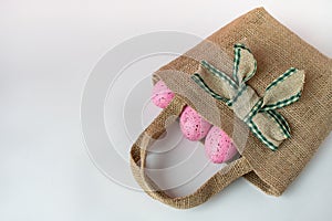 Pink spotted eggs in a rustic jute satchet on white background. Celebratory Easter wallpaper