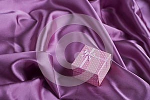 Pink squared gift box on purple satin fabric folds