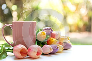 Pink steaming cup of hot coffee on white wooden near window with tulip flowers