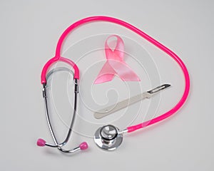 Pink stethophonendoscope, satin ribbon and scalpel on white background.