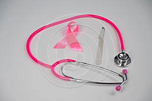 Pink stethophonendoscope, satin ribbon and scalpel on white background.