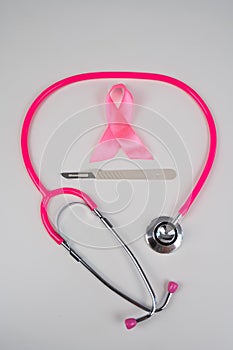 Pink stethophonendoscope, satin ribbon and scalpel on white background.