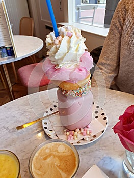 Pink strawberry freakshake with sweets, donuts and wipped cream in cafe, extreme milkshake