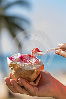 Pink strawberry ice cream in man`s hand in front of beach with p