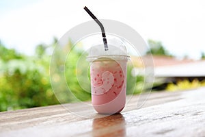 Pink strawberry milk pink ice drink in plastic cup juice for summer and straw on wooden table with nature