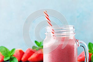 Pink strawberry smoothie or milkshake in mason jar on turquoise table. Healthy food for breakfast and snack.