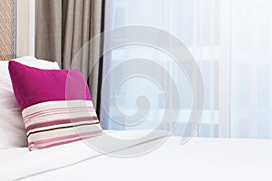 Pink stripe pillow on white bed in a brightly lit bedroom