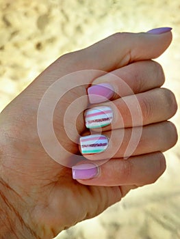 Pink striped manicure on a background of golden sea sand. Manicure idea for a vacation at sea. Gel nail design