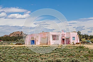 Pink stucco house in sagebrush field with mountian-rock formation and other houses in background in US Southwest