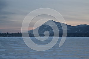 Pink Sunrise over a snowy mountain peak with frozen lake in the